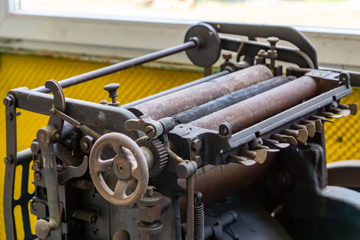 Close-up of a vintage letterpress machine with inked rollers and a hand wheel