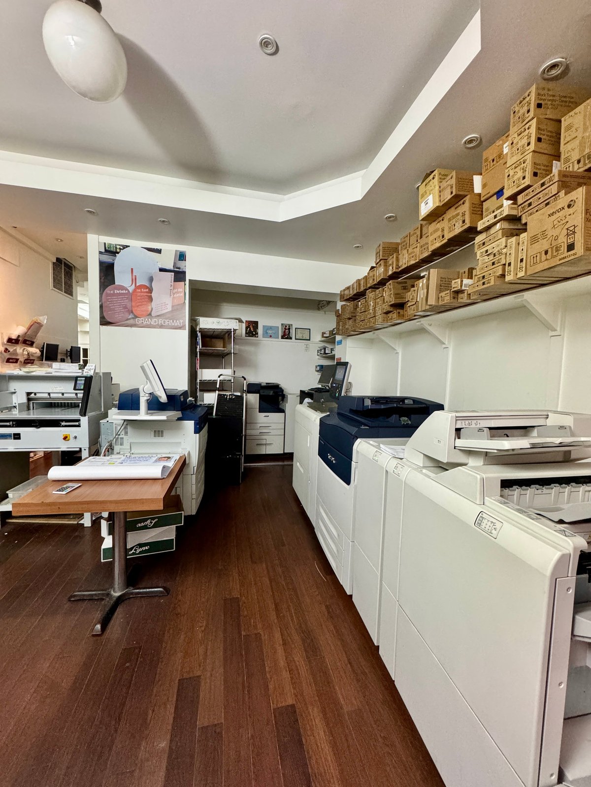 Print room at Copies Concordia with production copiers, paper stock on high shelves and a work table